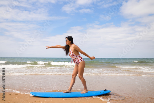 Beautiful young latin woman surfing with blue surfboard. The woman is on the beach. Holiday and summer concept.