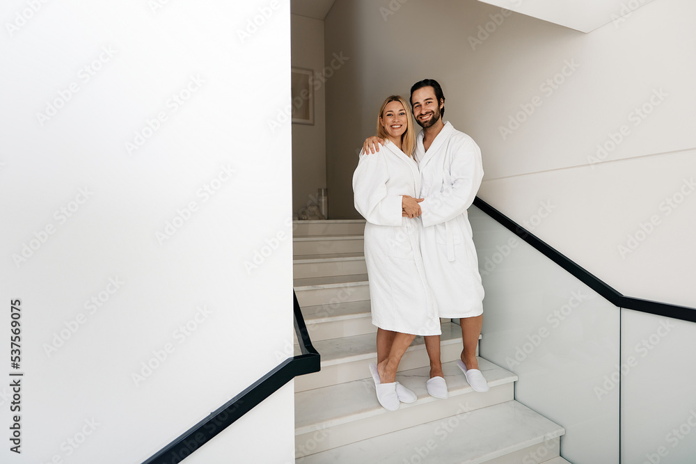 Spa family day. Handsome man with his beautiful wife in white bathrobes enjoying spa weekend while honeymoon walking at wellness center Spa family day. Handsome man with his beautiful wife in white bathrobes enjoying spa weekend while honeymoon walking at wellness center
