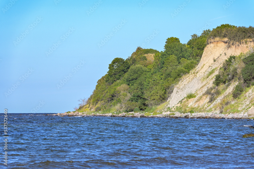 Steep coast with shrub vegetation and erosion of clay and boulders on the Baltic Sea near the tourist resort Steinbeck, Boltenhagen, Germany, blue water and clear sky, copy space Steep coast with shrub vegetation and erosion of clay and boulders on the Baltic Sea near the tourist resort Steinbeck, Boltenhagen, Germany, blue water and clear sky, copy space