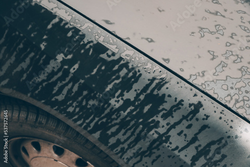 Close-up picture of stains on dark grey tin of a wet car bonnet and wheel detail. Color abstract photo of water drops surface.
