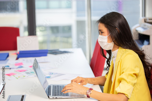 Asian business woman wearing surgical mask working with laptop in office. new normal lifestyle at workplace. 