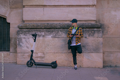 Man with a electric scooter works remotely with tablet at night