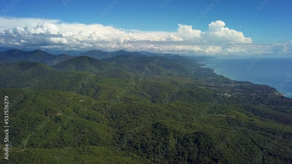 aerial view during the flight over the Black Sea coast - rain clouds over the green, forested, mountains of the Caucasus, illuminated by the sun against the blue sky aerial view during the flight over the Black Sea coast - rain clouds over the green, forested, mountains of the Caucasus, illuminated by the sun against the blue sky