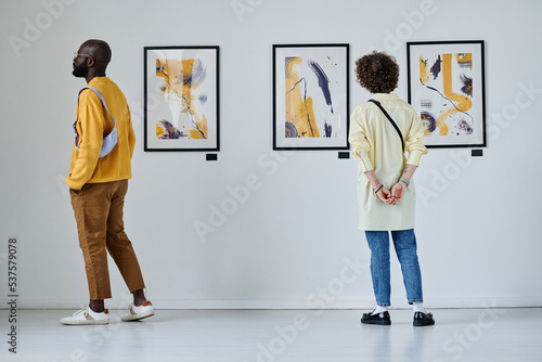 Rear view of young people looking at paintings on the wall at art gallery photo