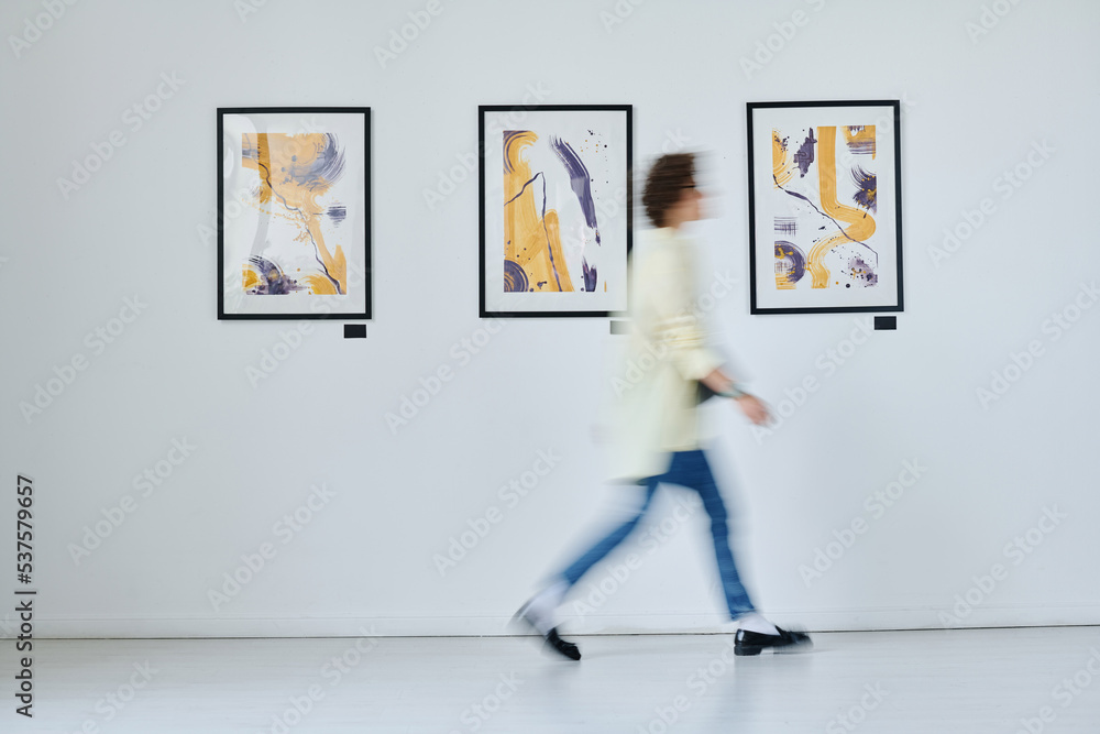 Blurred motion of young woman walking along art gallery with modern art on the wall - obrazy, fototapety, plakaty 