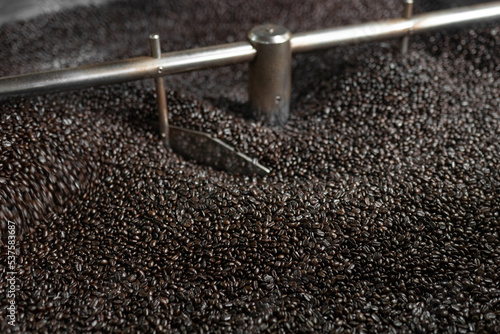 Dark roasted coffee grains being mixed inside of a roaster machine cooling tray