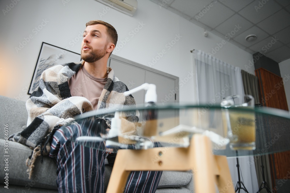 It's cold at home in wintertime. Man freezing in his house in winter because of broken thermostat. young guy wrapped in woolen plaid shivering while sitting on sofa in living room interior It's cold at home in wintertime. Man freezing in his house in winter because of broken thermostat. young guy wrapped in woolen plaid shivering while sitting on sofa in living room interior