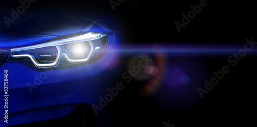Car headlights with light rays and copy space, banner. Neon light of car headlights on a dark background with lens flare, panorama, close up .