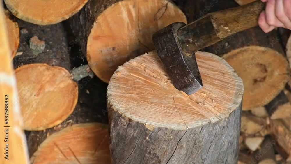 A man is chopping logs with an axe on chopping block. Harvesting of firewood stocks for heating. An alternative source of thermal energy instead of natural gas. A man is chopping logs with an axe on chopping block. Harvesting of firewood stocks for heating. An alternative source of thermal energy instead of natural gas.