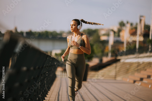 Fotografia Active young beautiful woman running on the promenade along the riverside