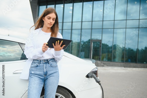 Wallpaper Mural Woman near electric car. Vehicle charged at the charging station. Torontodigital.ca