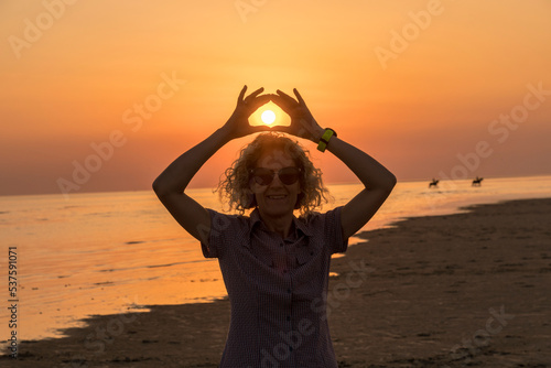 Blonde woman with sunglasses in front of the sun in the sunset
