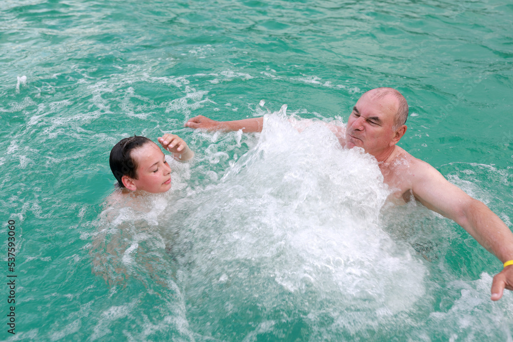 Grandfather and grandson get hydromassage in thermal pool