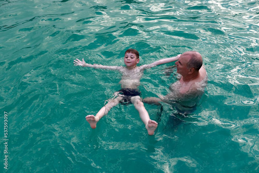 Grandfather teaches grandson to swim on his back in thermal pool
