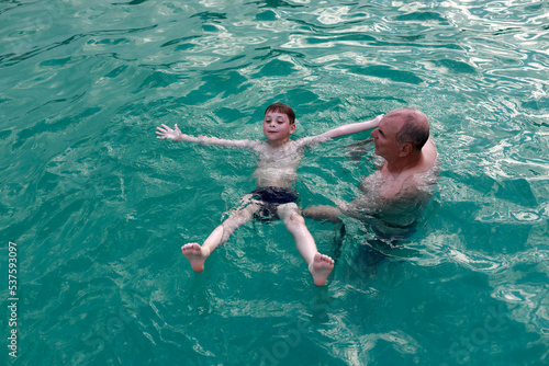 Grandfather teaches grandson to swim on his back in thermal pool photo