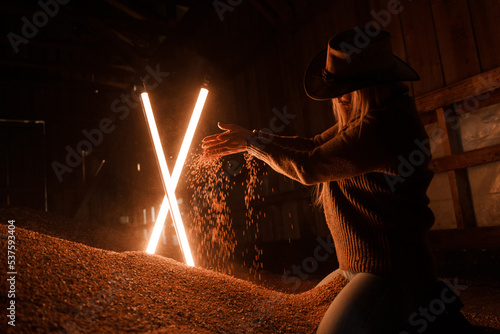 Shot of female farmer with cowboy hat scattering grains in dark hangar.