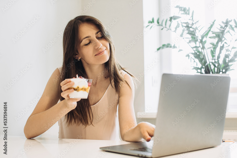 The concept of working at home. Young woman with a laptop in the kitchen, working with pleasure and eating delicious ice cream. The concept of working at home. Young woman with a laptop in the kitchen, working with pleasure and eating delicious ice cream.