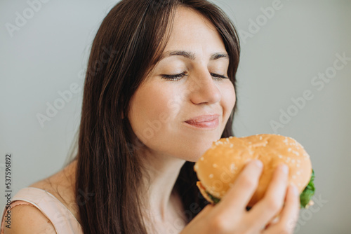 A beautiful young brunette woman is eating a tasty hamburger.