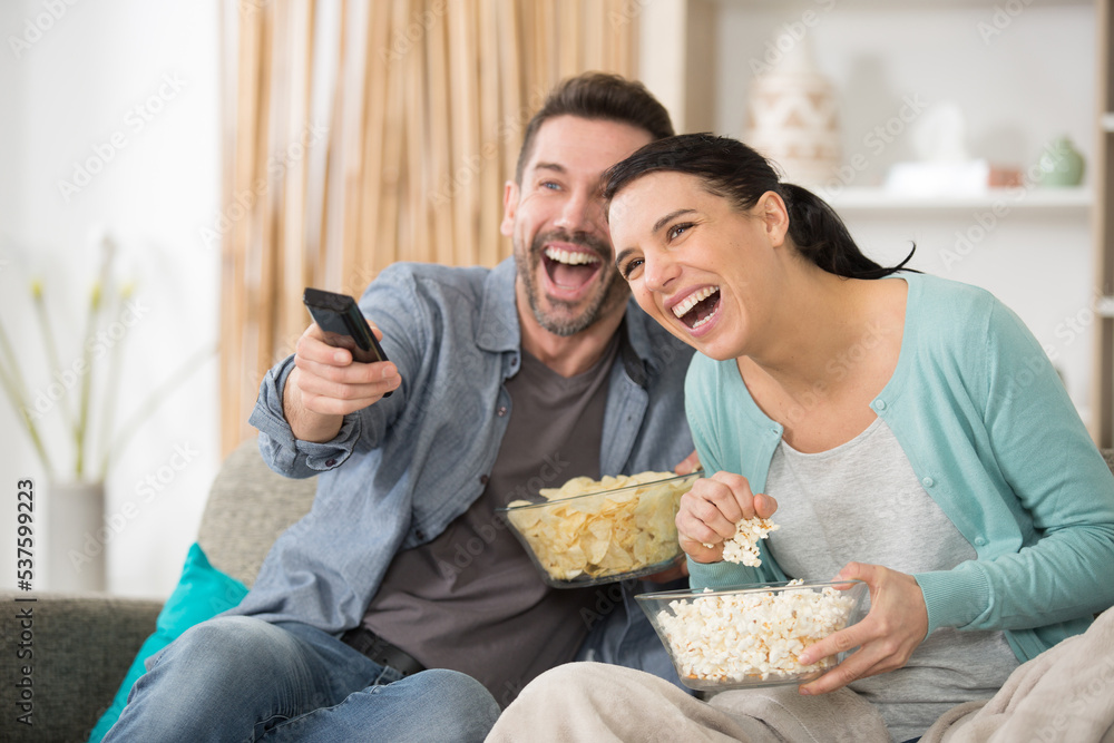happy couple with snacks watching tv on sofa at home