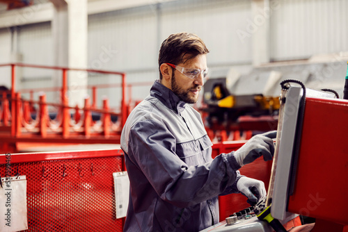 A heavy industry worker controls the machine and looks at the display while standing in the facility.