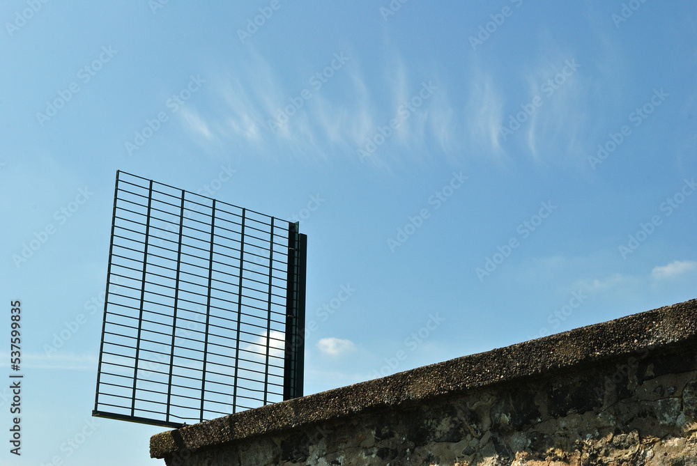 Stone Wall and Security Fence seen against Blue Sky with Patterned Feathery Clouds Stone Wall and Security Fence seen against Blue Sky with Patterned Feathery Clouds