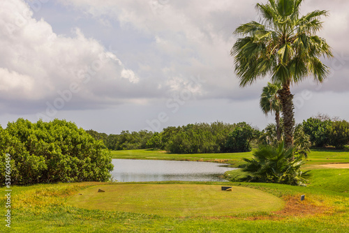 Beautiful view of nature landscape with golf course spot in front of little pond. Green bushes and pale blue sky on background. Aruba. 