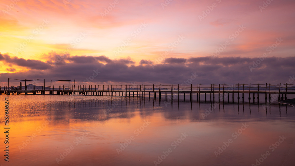 Wooden jetty on Carmoli beach at a beautiful and colorful sunrise, in Cartagena, Region of Murcia, Spain