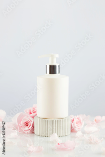 Dispenser white bottle on marble podium with tender pink roses and rose petals. Natural beauty product based on rose flowers  fermented cosmetic. Soft focus style  copy space  vertical format