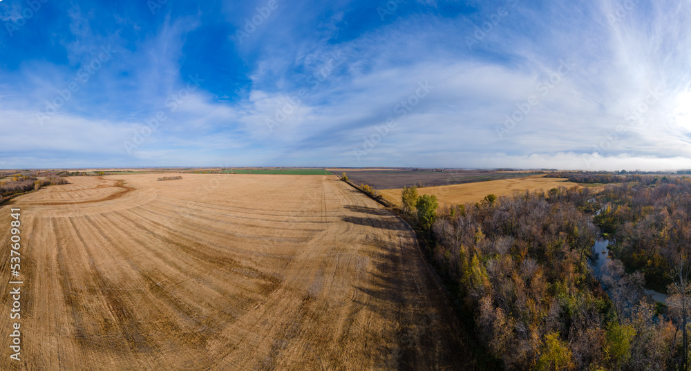 Obraz premium Drone panorama view above autumn farmland and a forest with a small river under a blue sky with white clouds. 