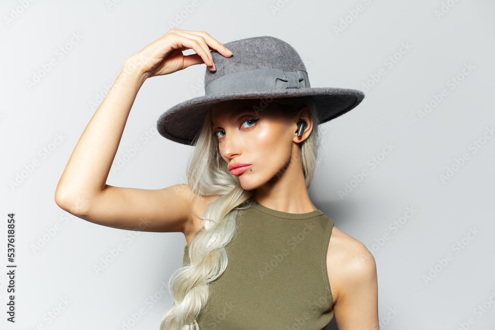 Studio portrait of young blonde attractive girl with earbuds in ears on white background, wearing grey hat. Studio portrait of young blonde attractive girl with earbuds in ears on white background, wearing grey hat.