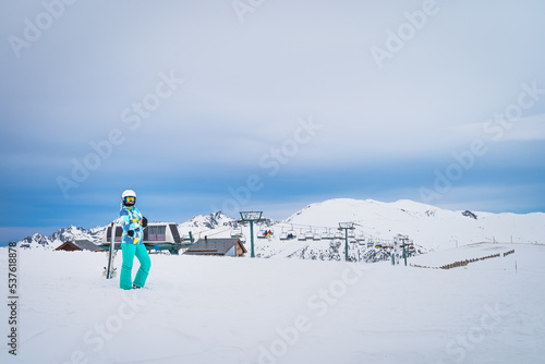 Portrait of a woman skier looking at a camera on the top of snowy Pyrenees Mountains with a ski lift in background. El Tarter, Grandvalira, Andorra