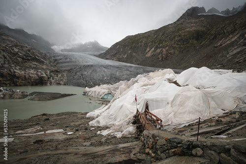 Scenic view on Rhone Glacier in swiss Alps with the lake. Rainy weather. High mountains landscape, arid terrain of Rhonegletscher, mountain trail in Switzerland. photo