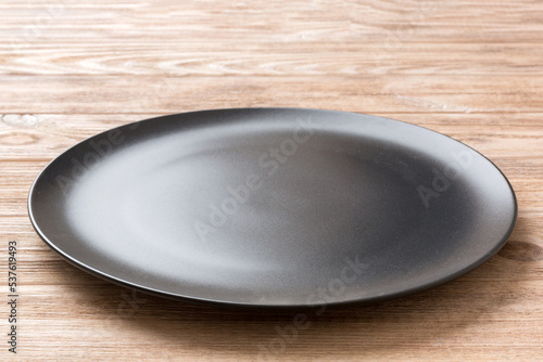 Perspective view of empty black plate on wooden background. Empty space for your design