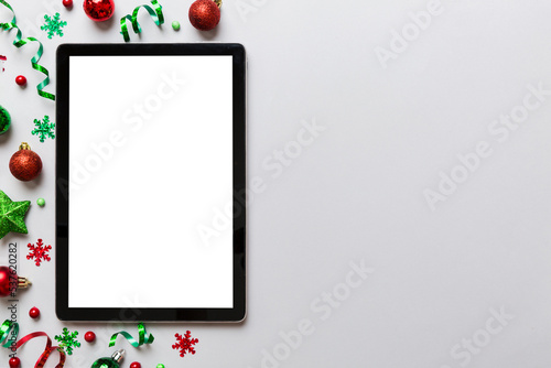 Christmas online shopping from home tablet pc with blank white display top view. Tablet with copy space on colored background with Christmas decorations balls . Winter holidays sales background