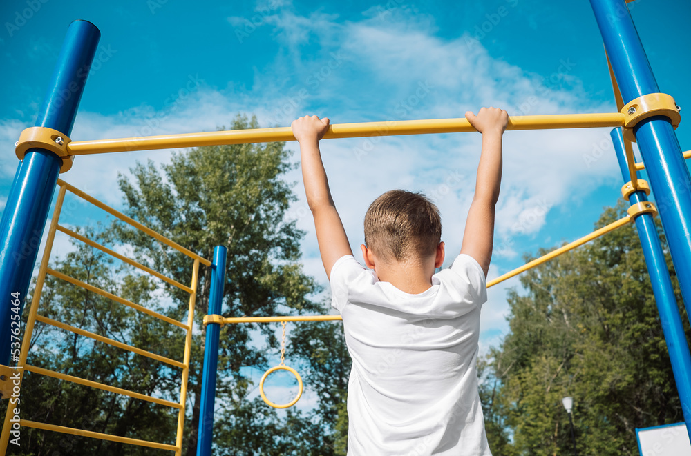 child hangs on the crossbar against the blue sky, view from the back. Selective focus