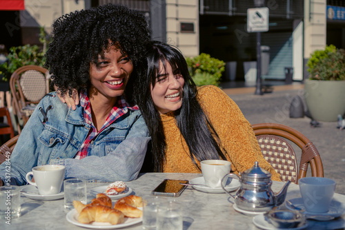 young latina and haitian afro woman laughing together embracing in an outdoor cafe in autumn