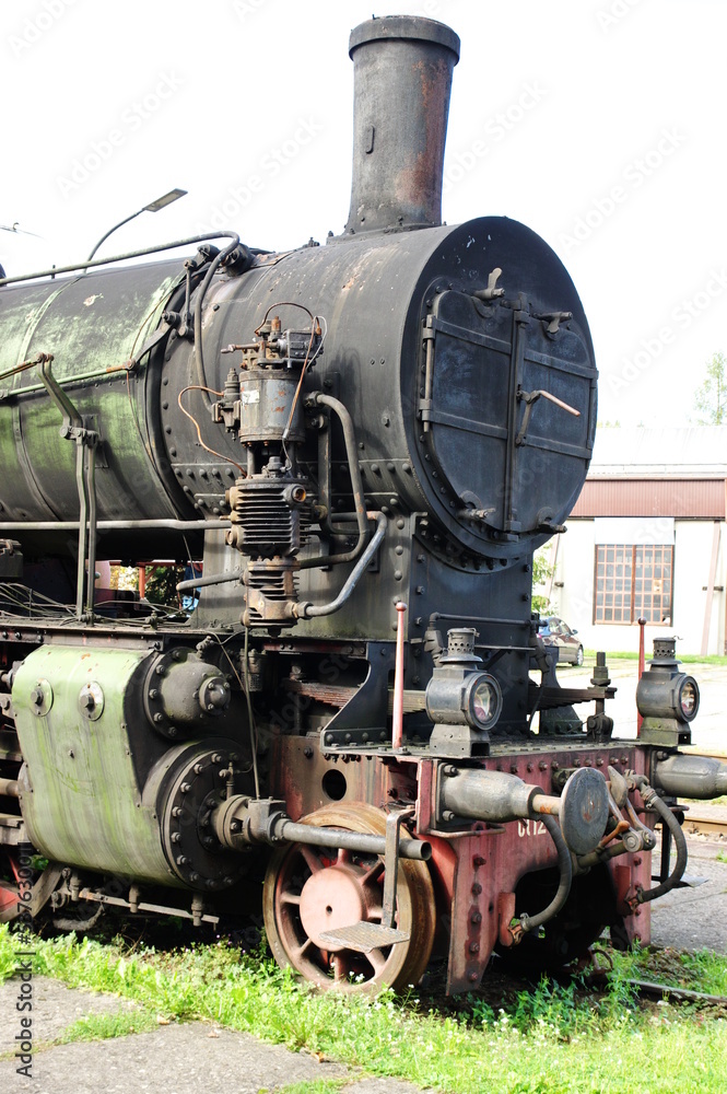 Naklejka premium Historic railway.The front part of a steam locomotive. A fragment of the boiler, wheels, pistons, lantern and bumper are visible.