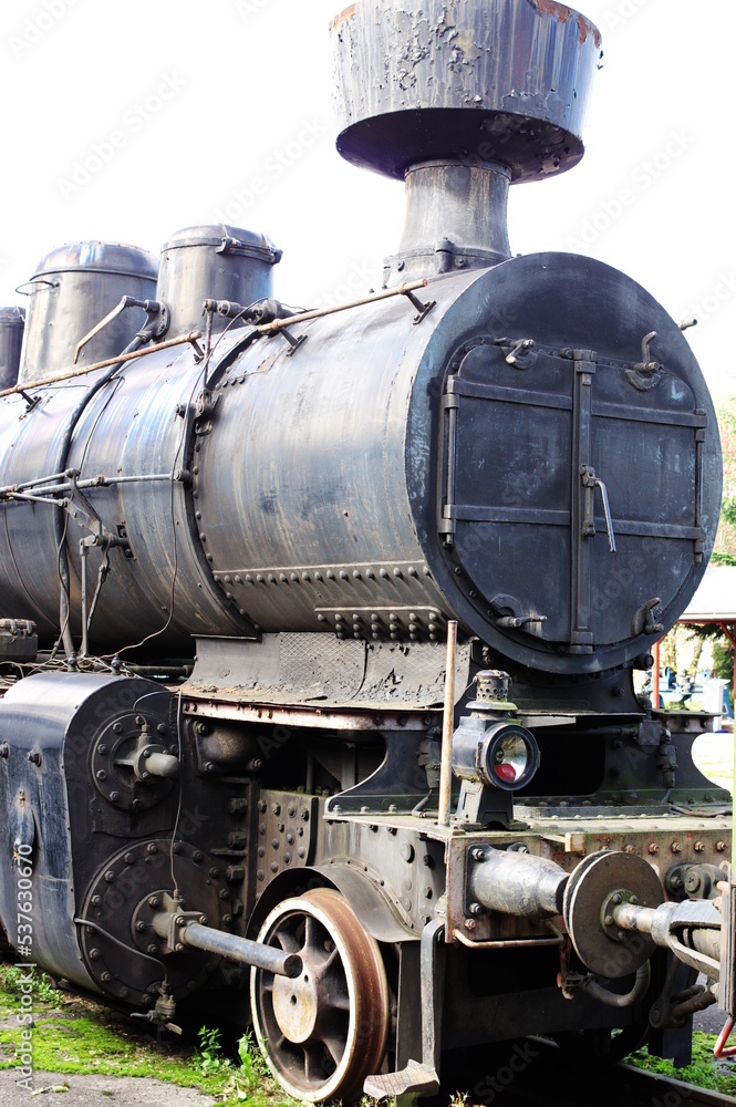 Naklejka premium Historic railway. The front part of a steam locomotive. A fragment of the boiler, wheels, pistons, lantern and bumper are visible.