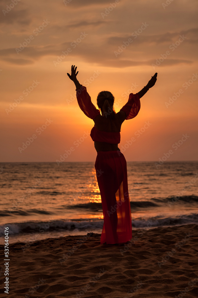 Silhouette middle aged woman arms raised on tropical sea sunset. Female posing relaxing on summer beach at tropical background. Lady in beachwear long dress. Travel vacation concept. Copy text space