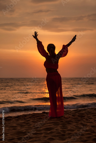 Silhouette middle aged woman arms raised on tropical sea sunset. Female posing relaxing on summer beach at tropical background. Lady in beachwear long dress. Travel vacation concept. Copy text space