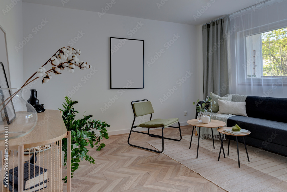 Fototapeta premium Modern interior of living room with comfortable sofa and armchair with table. Wooden floor in stylish room in apartment with window. Empty frame on the white wall.