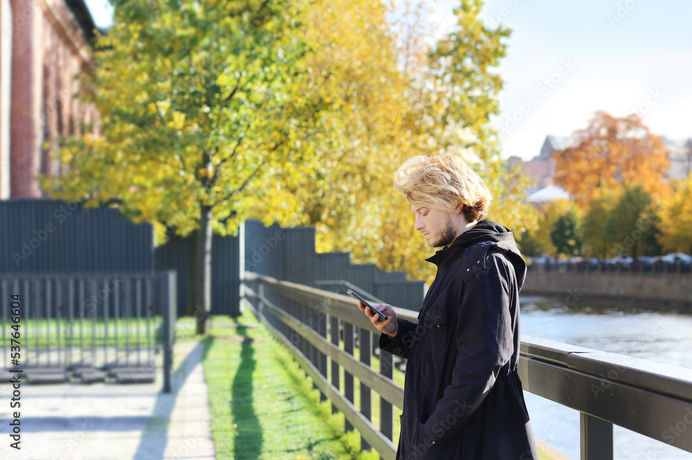 Fototapeta premium Lifestyle portrait of a young man using a smart phone outdoors. man relaxing in autumn park