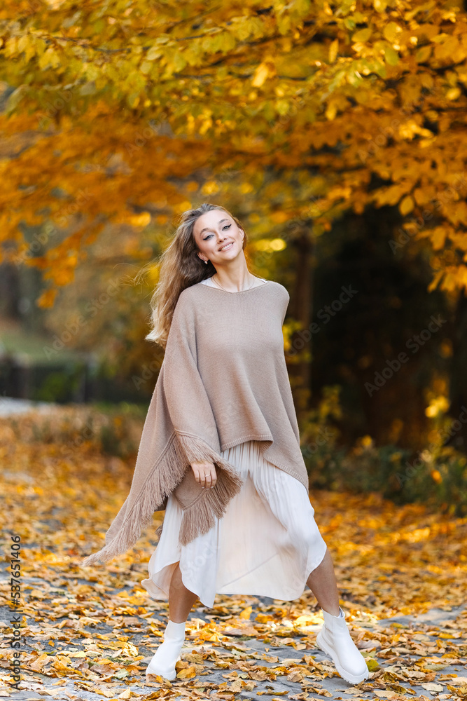 Playful woman in brown poncho enjoying autumn in the forest among yellow leaves. Playful woman in brown poncho enjoying autumn in the forest among yellow leaves.