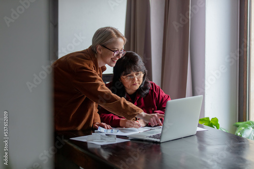 Two women count a bills with computer at home © Masson