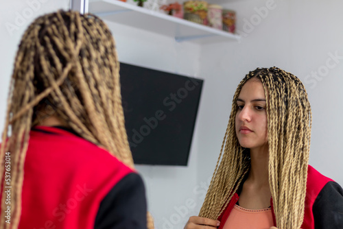 Teen girl standing in front of the mirror admiring the new hairstyle of boxing braids with kanekalon photo