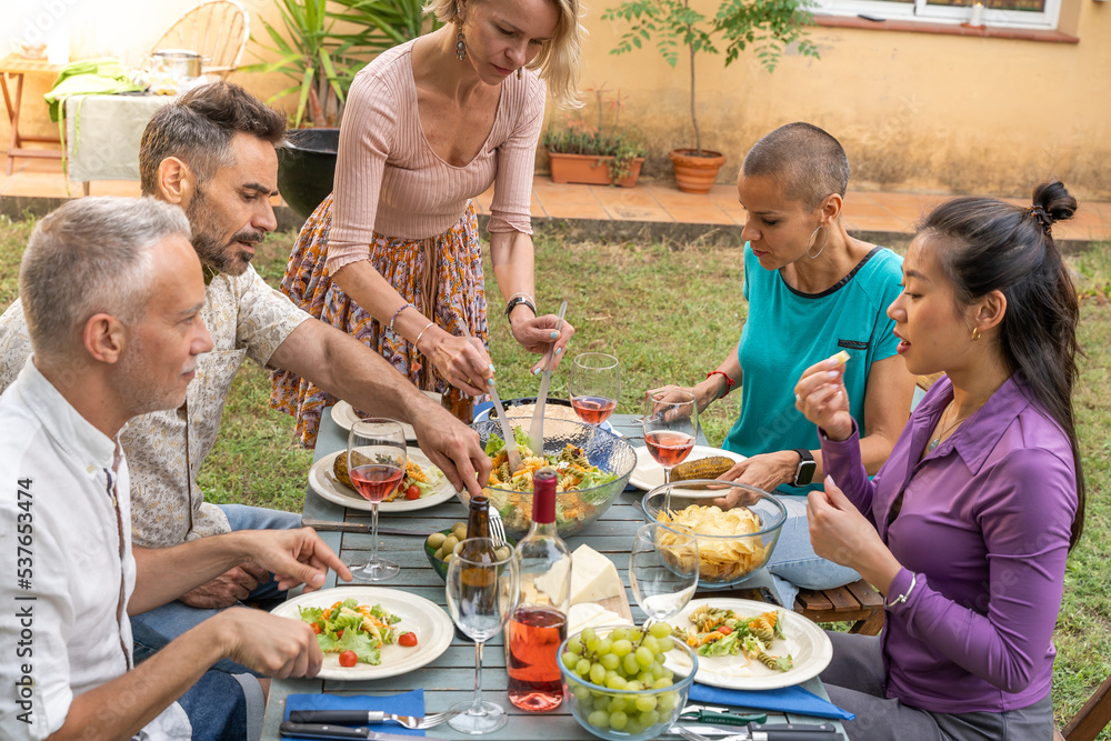 Woman serves the food with friends happy around the table.