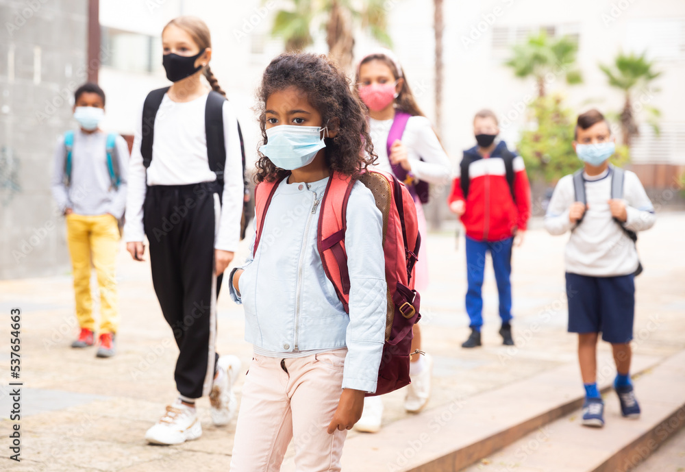 Obraz premium Portrait of tween girl in medical face mask on her way to college on warm autumn day. Forced precautions in COVID pandemic