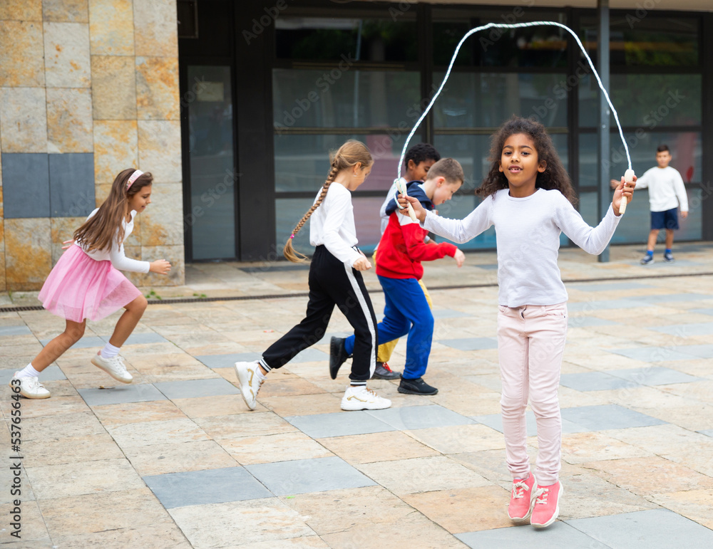 Cute tween African American girl skipping rope in schoolyard during break between lessons Stock