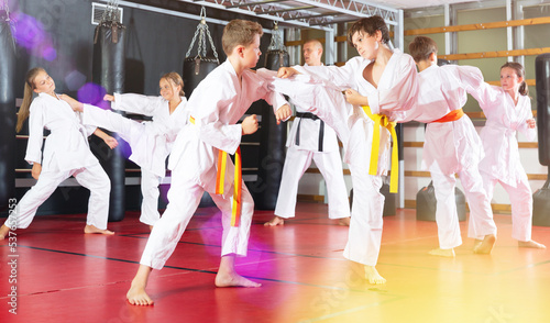 Group of preteen children practicing taekwondo kicks in pairs at sport gym