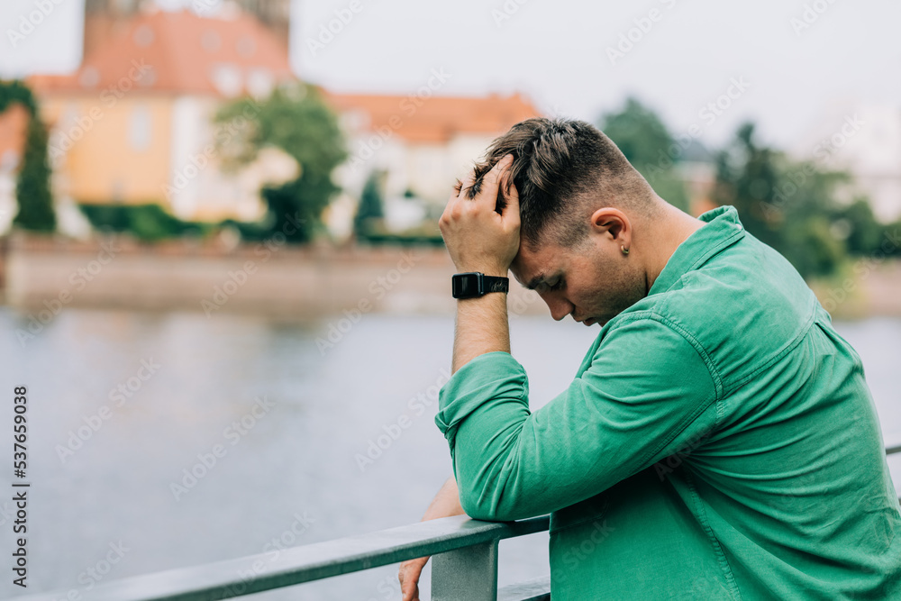 Young sad guy in green shirt keep hand on head and stand near river on Wroclaw, Poland Young sad guy in green shirt keep hand on head and stand near river on Wroclaw, Poland